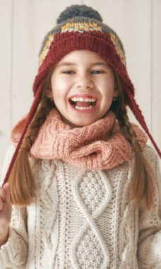 Winter portrait of happy little girl wearing knitted hat, scarf and sweater. Child on white wooden background. Fashion concept.